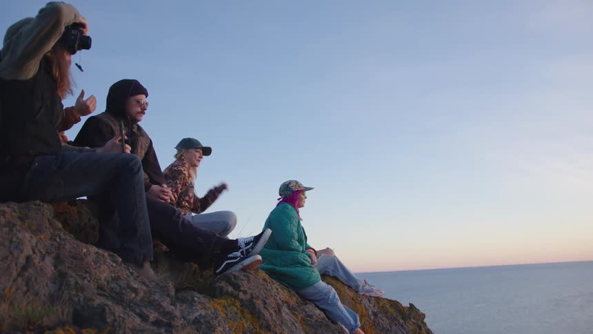Friends sit on the cliff looking over the water