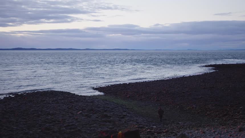 Aerial of the tide gently rolling in on the shoreline along the coast at dusk