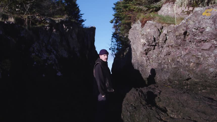 Man standing in a rocky crevice beneath a bright sky