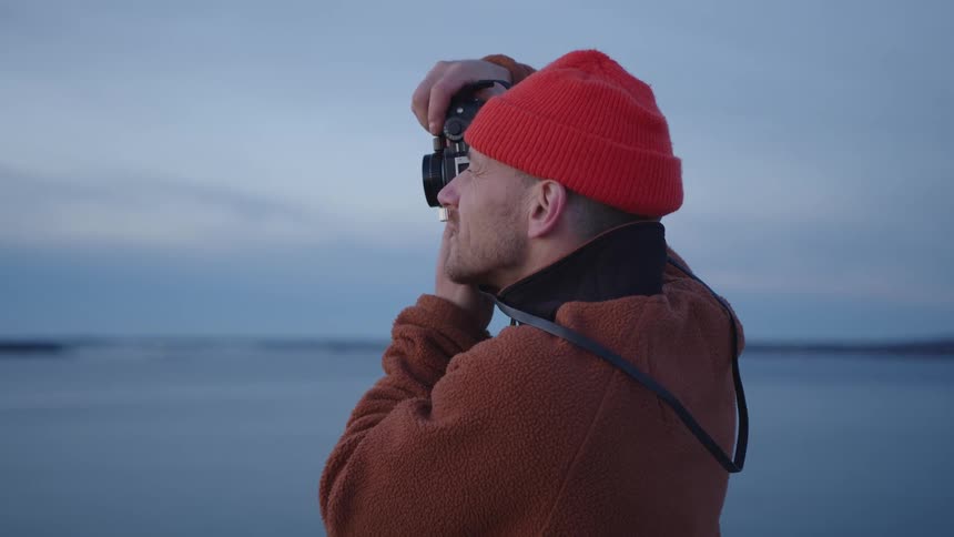 Man photographing a calm waterfront under an overcast sky