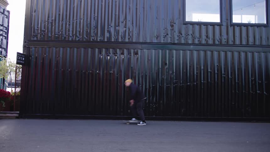 Skateboarder in motion on paved ground in front of black metal wall