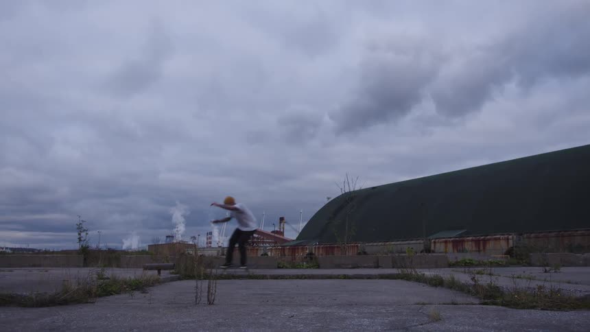 A man rides a skateboard across a concrete pavement on a cloudy day gliding steadily beneath the overcast sky