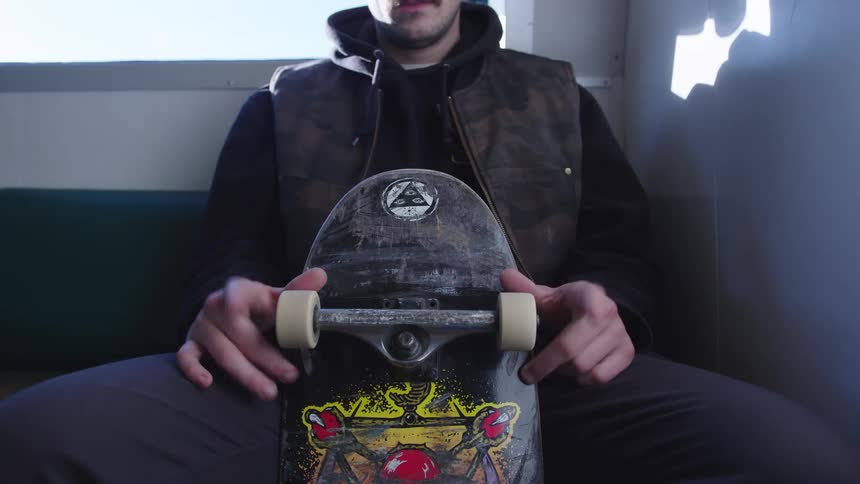 A man sits holding his skateboard
