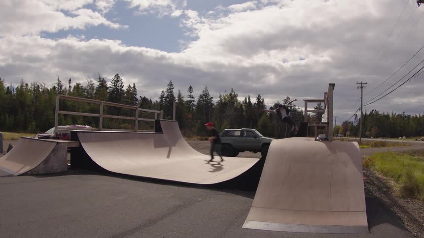 Two skateboarders perform tricks on an outdoor wooden ramp