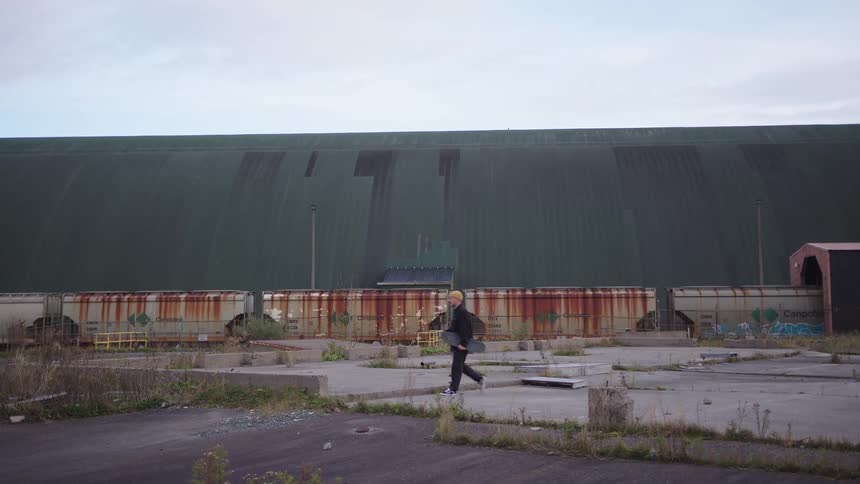 A man walks on a concrete platform at midday holding a skateboard