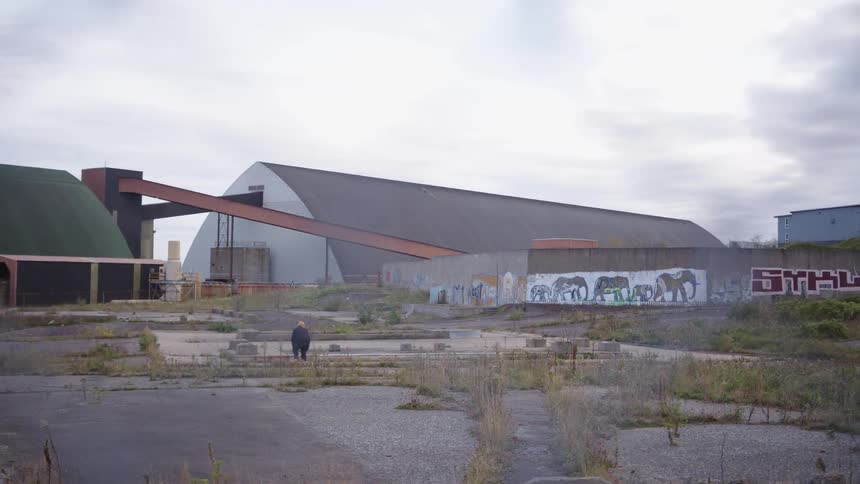 A man skateboards behind in an abandoned lot