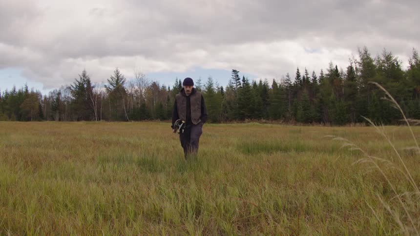 Man holding skateboard walking through grassland outdoors