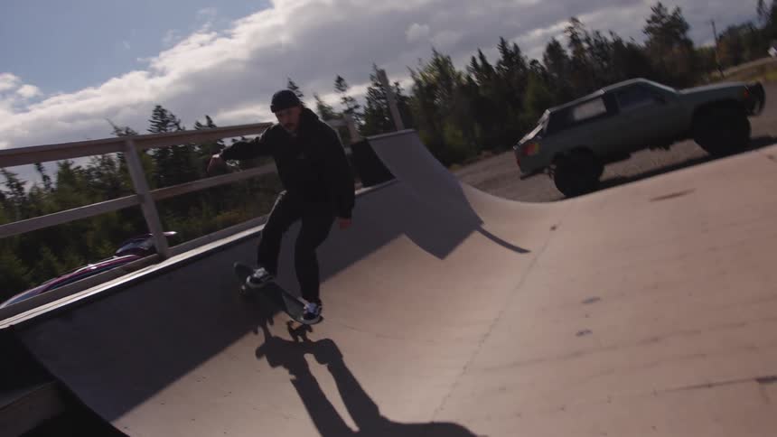 Skateboarder performs a trick on an outdoor ramp under a partly cloudy sky