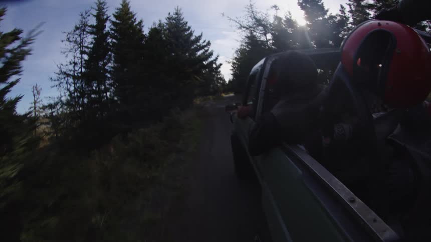 The video is a lowangle shot from the bed of a green pickup truck driving quickly down a narrow treelined dirt road the scene is bright with sunlight peaking through the dense forest canopy