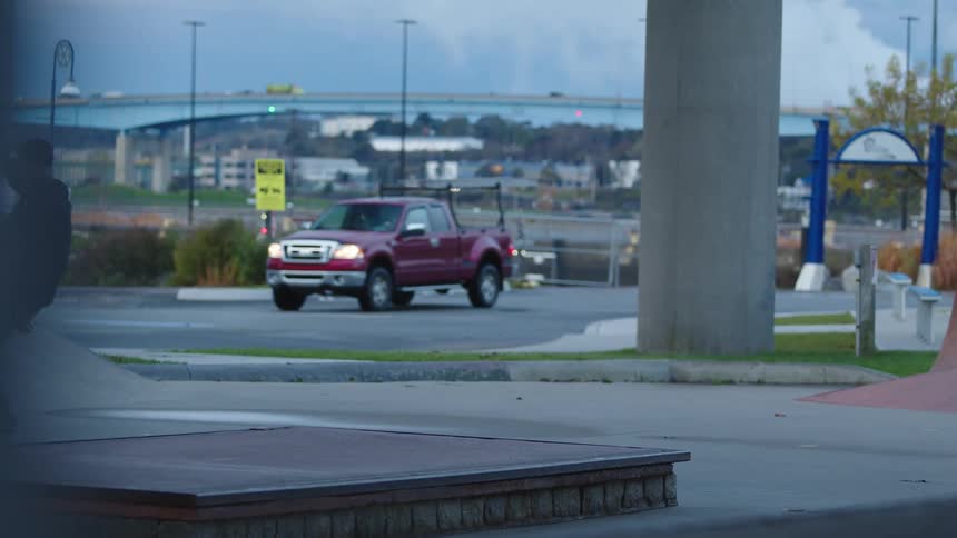 Man skateboards in an urban park with bridge and traffic in background