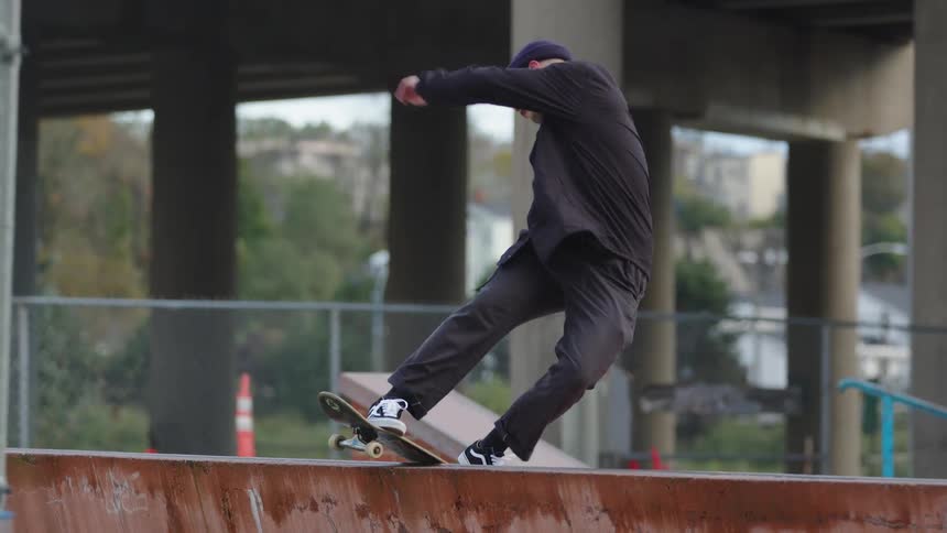 Skateboarder slides along a rail at a skate park under an overpass