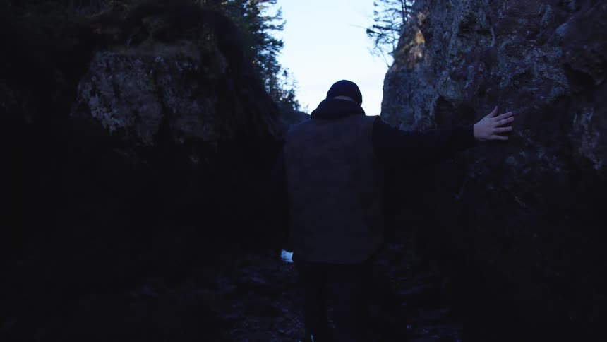 Man walks between damp rocks toward the view of the sea in the distance