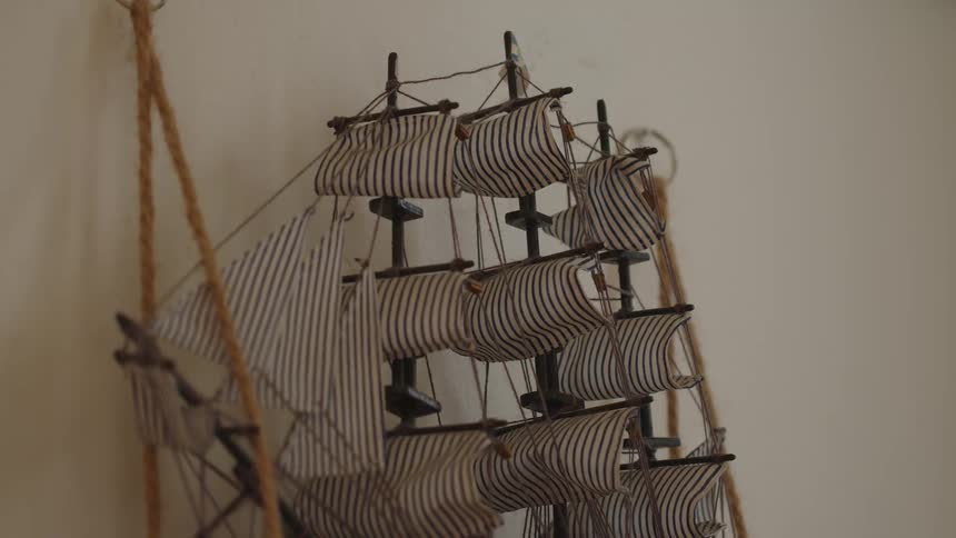 A detailed miniature sailing ship with striped sails stands against a neutral wall