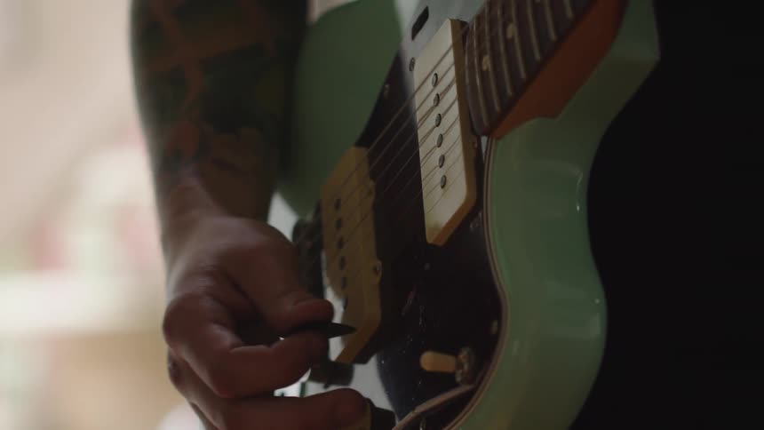 Hand plucking the strings of a green electric guitar in closeup