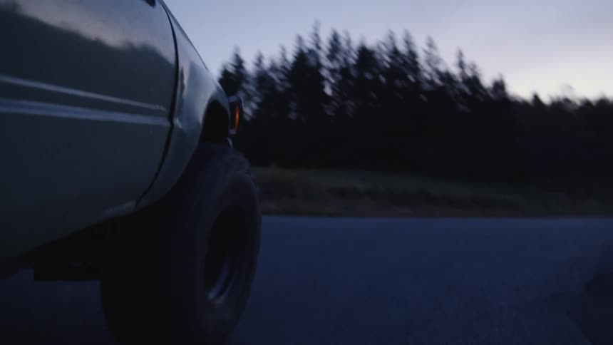 A truck cuts to the right at an intersection driving on a lonely road at sunrise with trees lining both sides