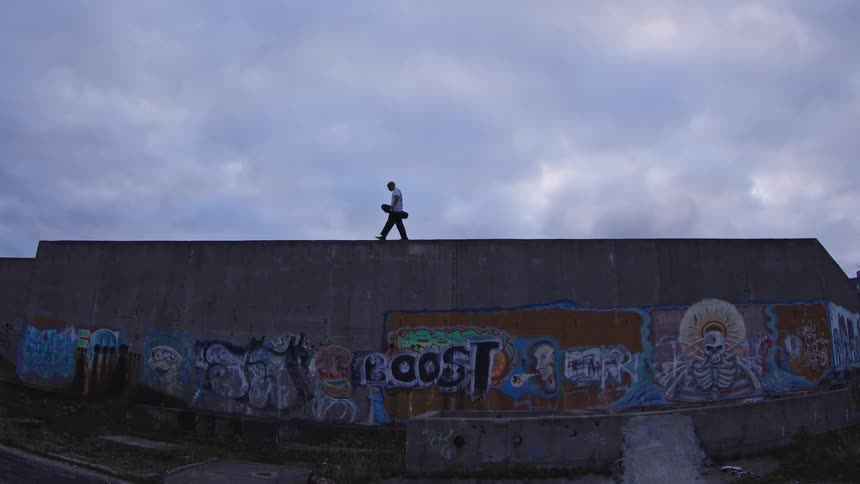 A young man carrying a skateboard while walking on a building during daytime