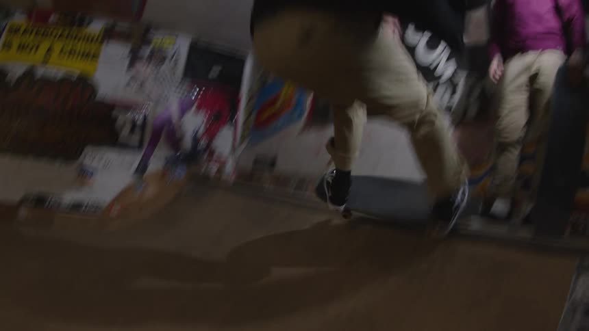 Skateboarder practicing tricks in an indoor ramp surrounded by posters and graffiti