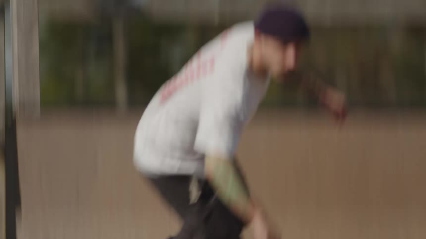 A close view shows a skateboarders feet wearing dark pants and white and black shoes as they drop into a wooden ramp at a skate park on a sunny day