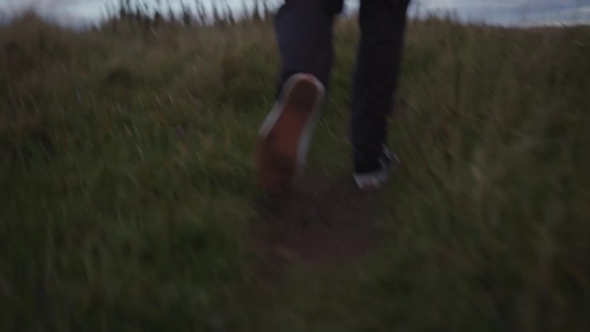 Close up of a young mans legs as he walking through a path on a grass field during daytime
