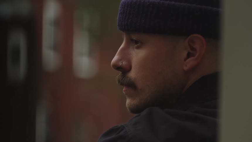A side profile of a man with a mustache and beanie in a city setting