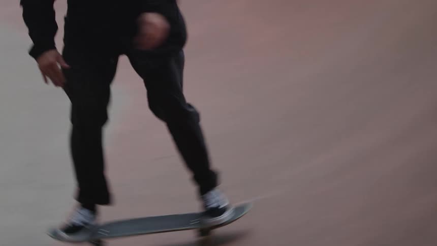 The video is a closeup of a person skateboarding on the flat bottom of a large curved skate ramp the camera follows their feet as they ride showing their black pants and sneakers as they glide over the smooth reddishbrown surface