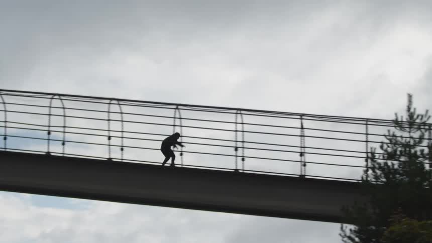 The man rides his skateboard and jumps on the overpass
