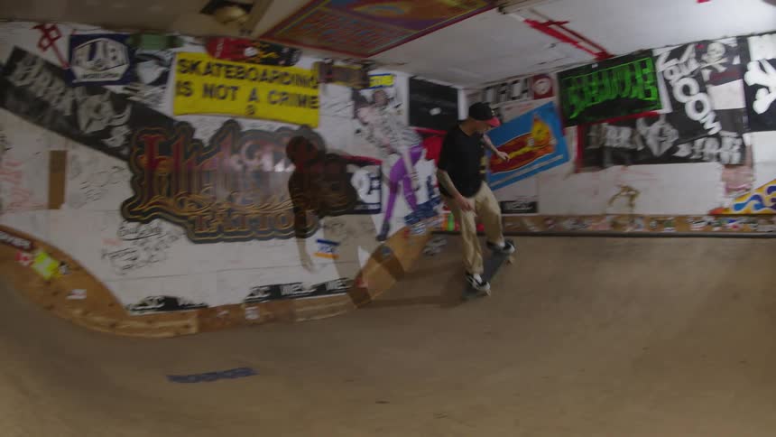 Skateboarder makes a turn in an indoor skate park decorated with posters and graffiti