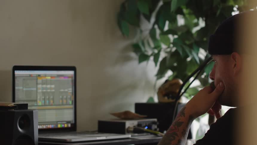 A young man sits in front of a computer screen watching the monitor with a flower plant beside him