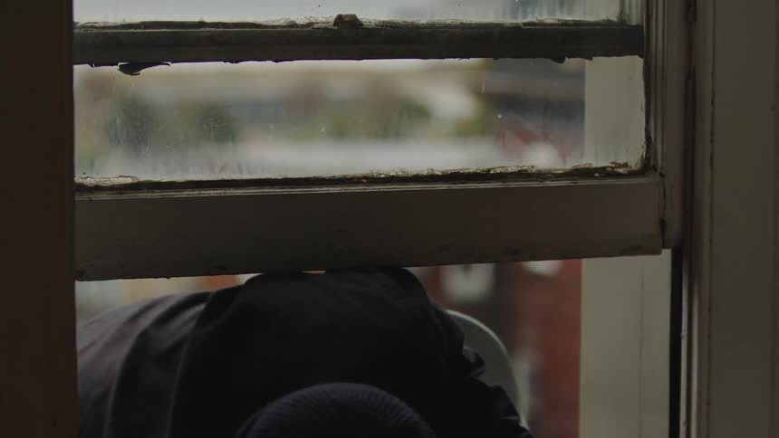 Male skateboarder climbs through a window with his skateboard on an autumn day