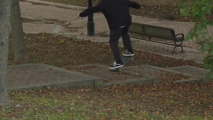 A man rides a skateboard down a public staircase in a park at midday