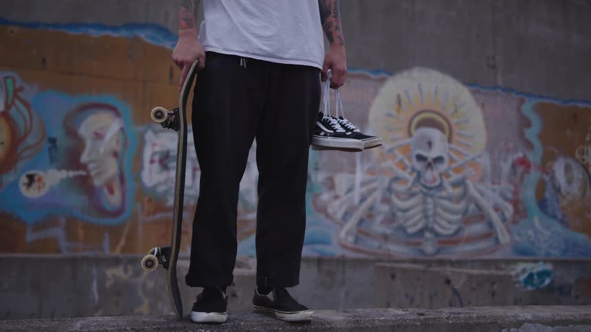Skater stands by a graffiti wall holding a board