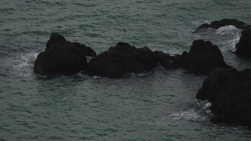 Ocean waves crash against a rocky shoreline at midday