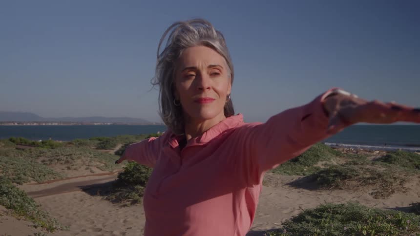 Grayhaired woman practices a balancing pose on a sunny beach