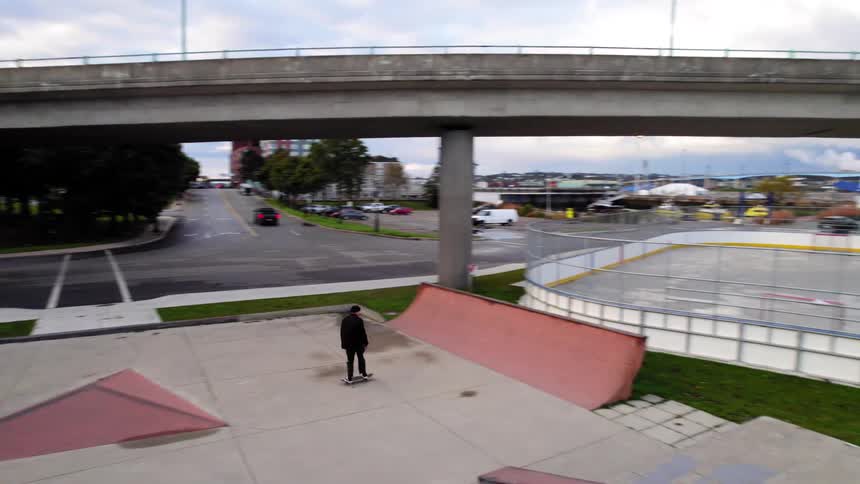 Skateboarder performs a trick on a ramp near an overpass overlooking the city