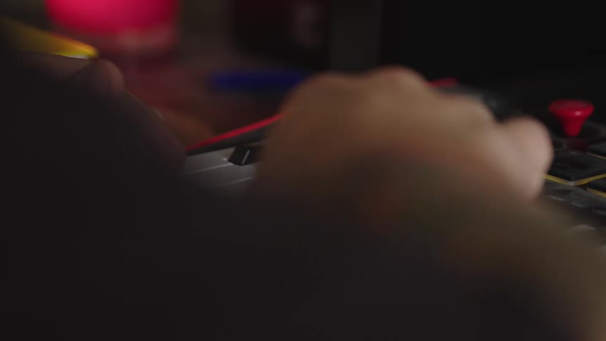 A persons hands move over and press the keys of a small electronic keyboard the keyboard has white and black keys red elements are visible on the sides and the scene is in an indoor setting