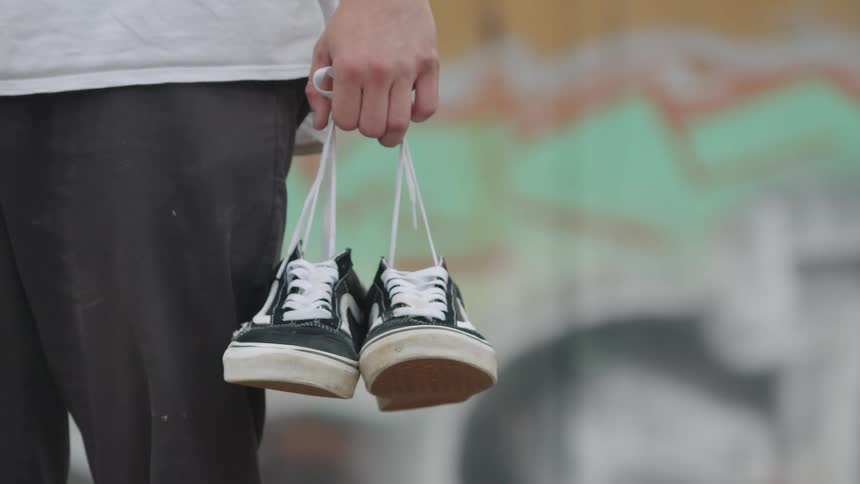 Person holding a pair of black sneakers with white laces by the hand