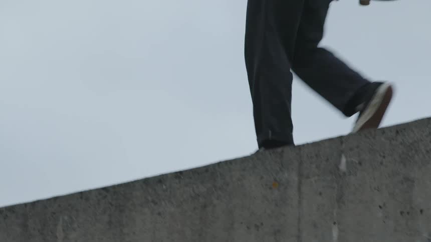 Man walking on the roof of a train car with a skateboard in his hand