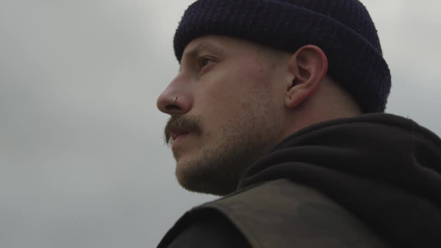 Man wearing a beanie looks toward the horizon under a cloudy sky