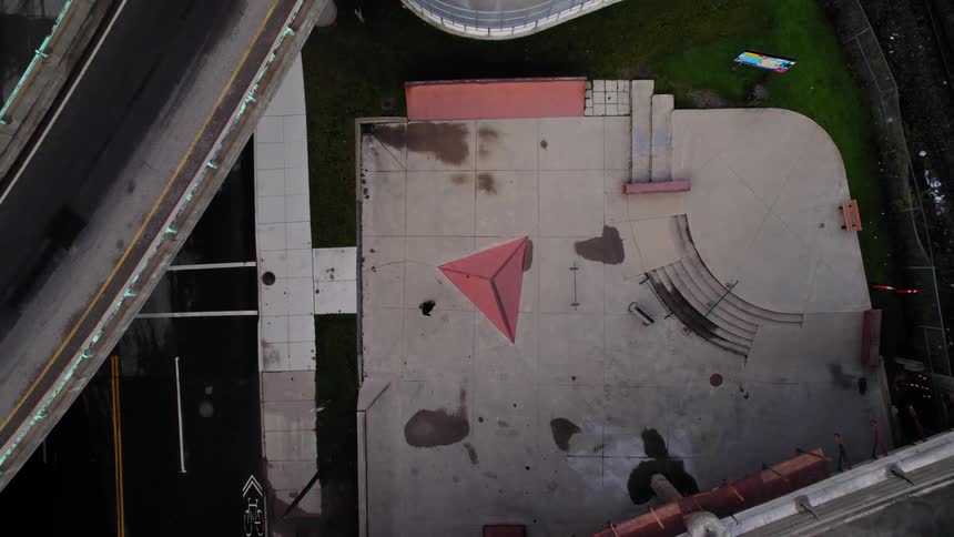 Aerial view of a skateboarder in a concrete skatepark beneath overpasses