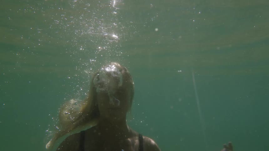 A young blonde woman swimming in a body of water during daytime