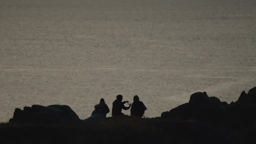 People are sitting on the rocks by the shore