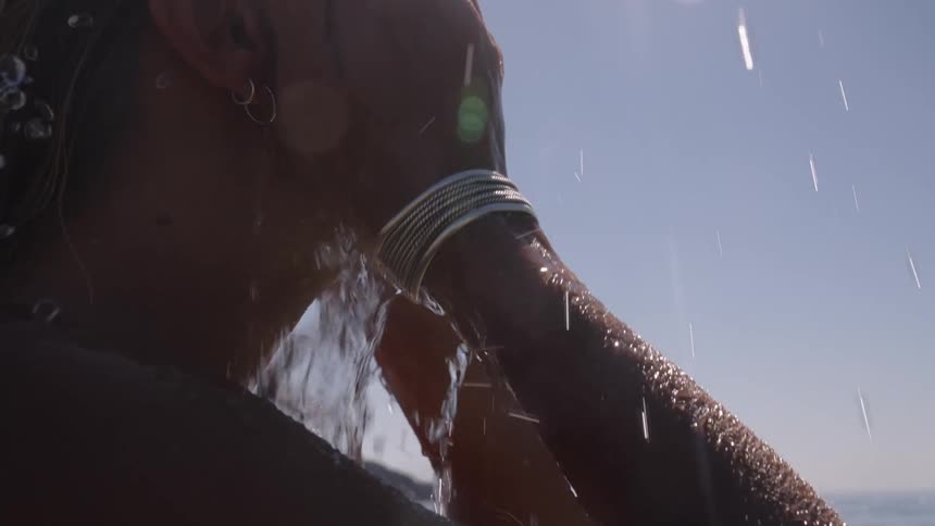 Woman refreshes herself by bringing seawater to her face under the bright sun
