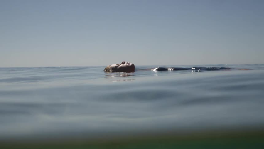 A young woman floats in the ocean on a sunny day her body submerged with only her face above the water