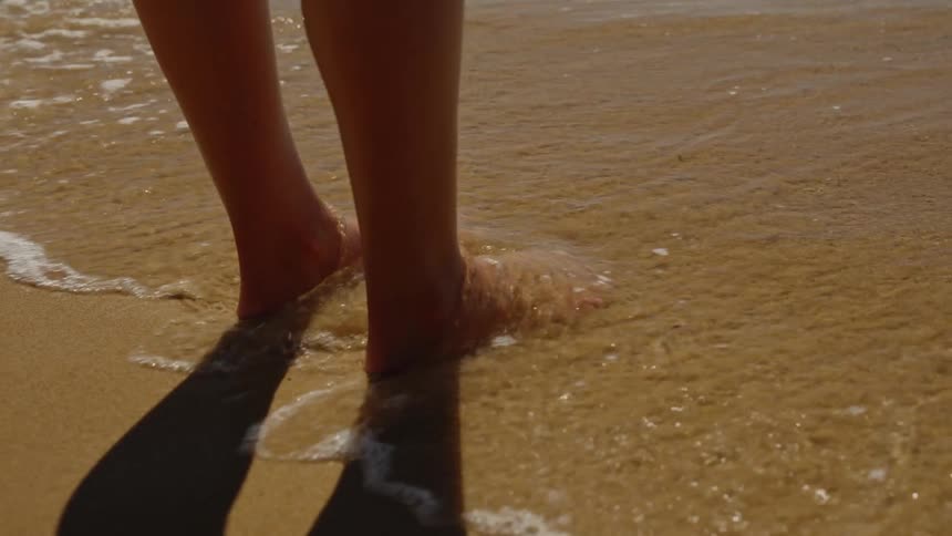 Feet touch the seawater as the tide washes over the golden sand