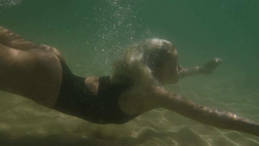 Woman swimming underwater in a black swimsuit with bubbles around her