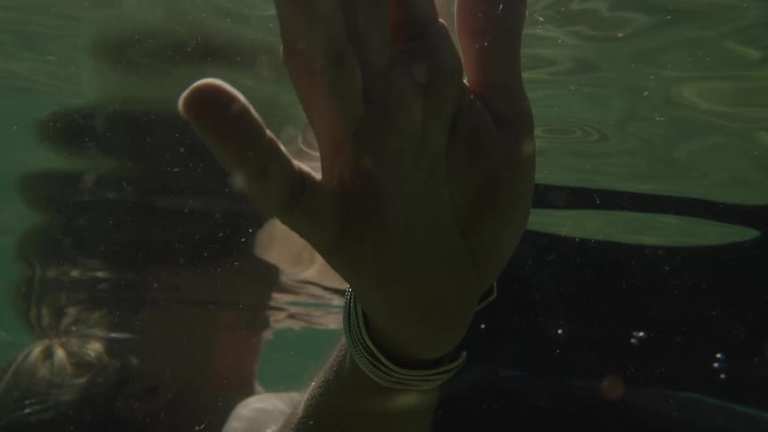 Woman wearing a swimsuit moves her hand through the water while floating on her back