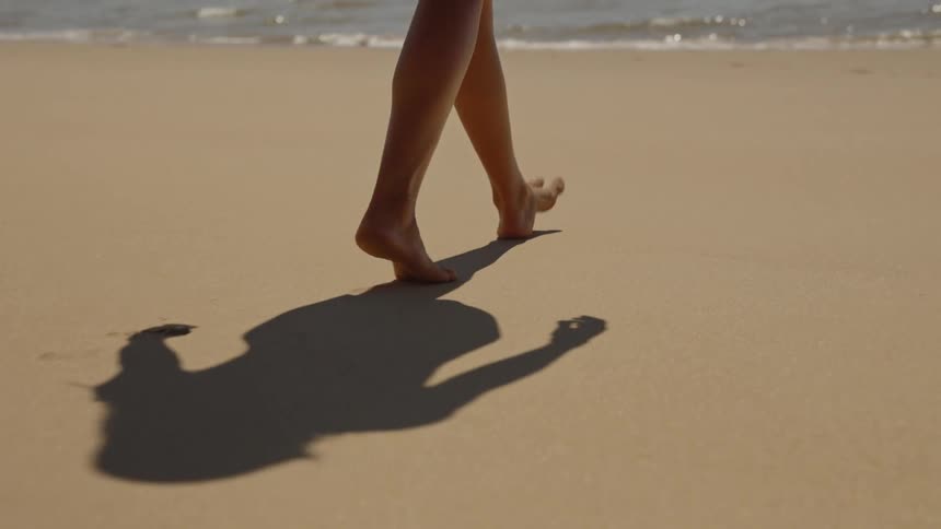 Bare feet walking on the sand with a shadow cast in the sunlight