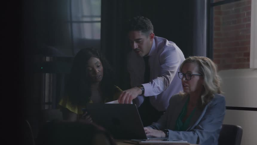 Man interacts with colleagues in office setting during meeting involving laptop papers and phone