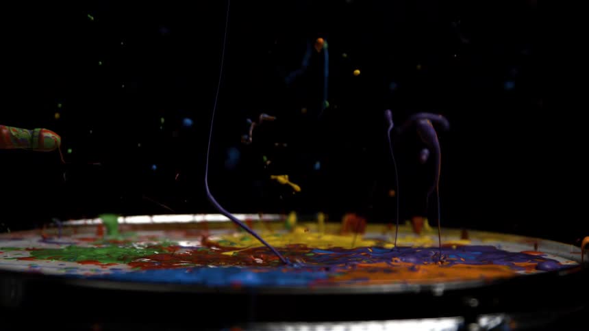 Colorful paint splashing upward as a drumstick strikes the surface