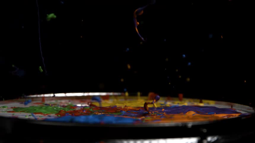 Colorful paint strands rise in slow motion from a surface